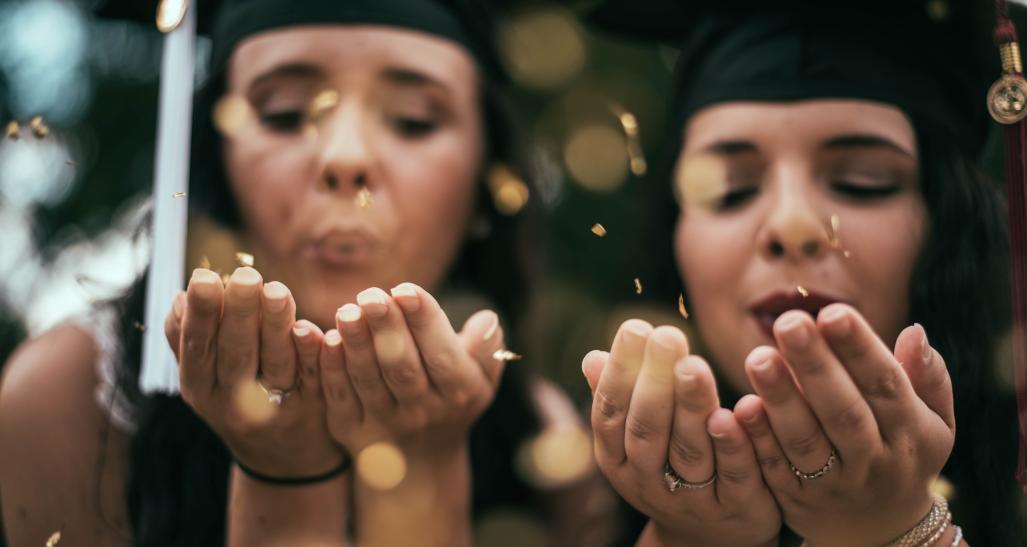 two female graduation students blowing confetti on their graduation day