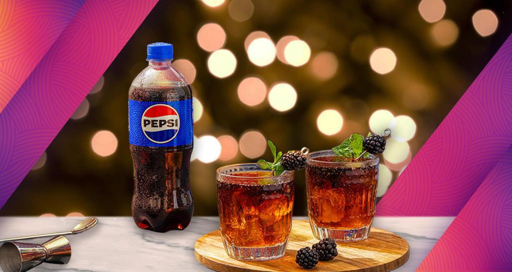 A bottle of Pepsi sits next a board with cocktails, with twinkling white lights in the background.