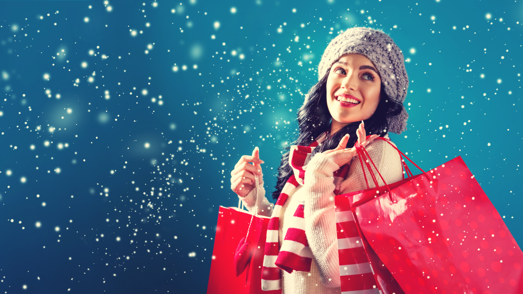 Woman wearing hat and scarf carrying red shopping bags in the snow